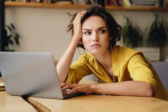 Young woman with concerned expression using laptop, reflecting on autistic teen punished by teacher for not reading sarcasm.