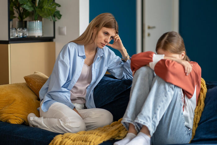 Worried mom talks with her upset autistic teen sitting on a couch after punishment for not reading sarcasm at school. Worried mom talks with her upset autistic teen sitting on a couch after punishment for not reading sarcasm at school.