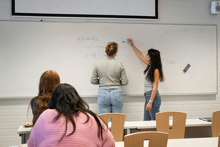 Students working together at a whiteboard in a classroom, discussing and writing notes during a study session.