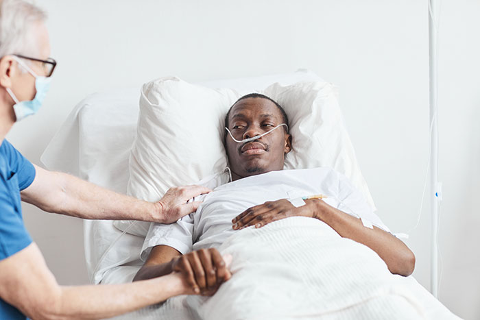 Patient in a hospital bed with oxygen tube, holding hands with a visitor, illustrating coma survivors' stories.
