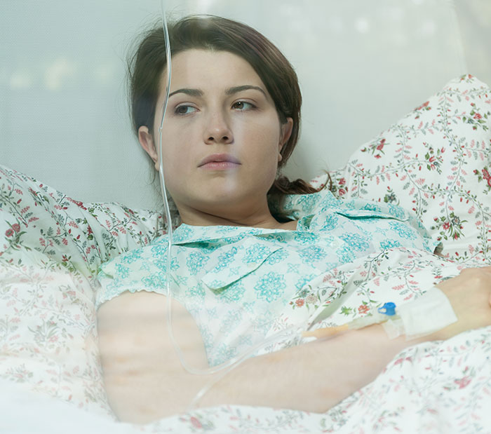 Young woman in hospital bed with IV, representing coma survivors sharing their stories and experiences.