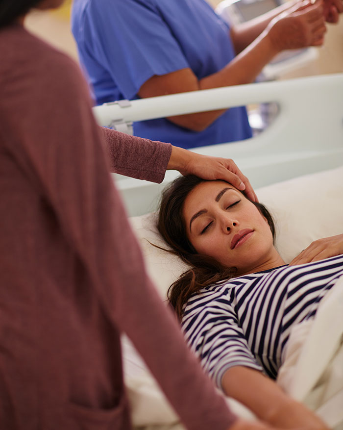 Patient lying unconscious in hospital bed with family member holding her head, illustrating coma survivors' stories.
