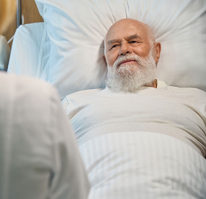Elderly man with white beard lying in hospital bed, symbolizing coma survivors sharing their recovery stories.