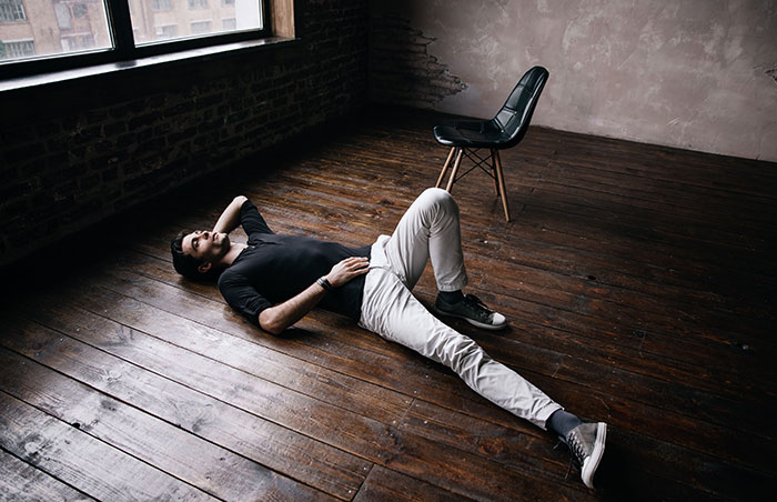 Man lying on wooden floor in empty room with chair nearby, symbolizing people who walked away and started new lives.