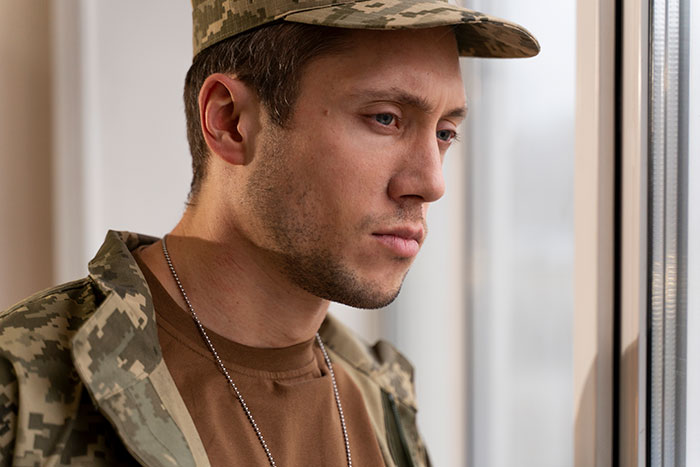 Young man in military uniform looking thoughtfully out window, reflecting on walking away from old life and starting new one.