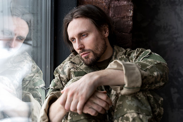 Man in military uniform sitting by a window, reflecting on his journey of walking away from his old life and starting anew.