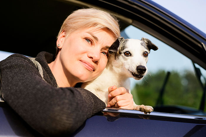 Woman with short blonde hair sitting in a car holding her dog, symbolizing people who walked away from their old lives.