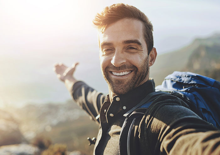 Smiling man with backpack taking a selfie outdoors, representing people who walked away from their old lives and started anew.