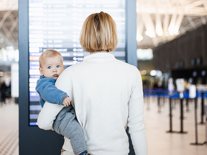 Adult carrying baby at airport terminal, symbolizing people who walked away from old lives to start a new one.