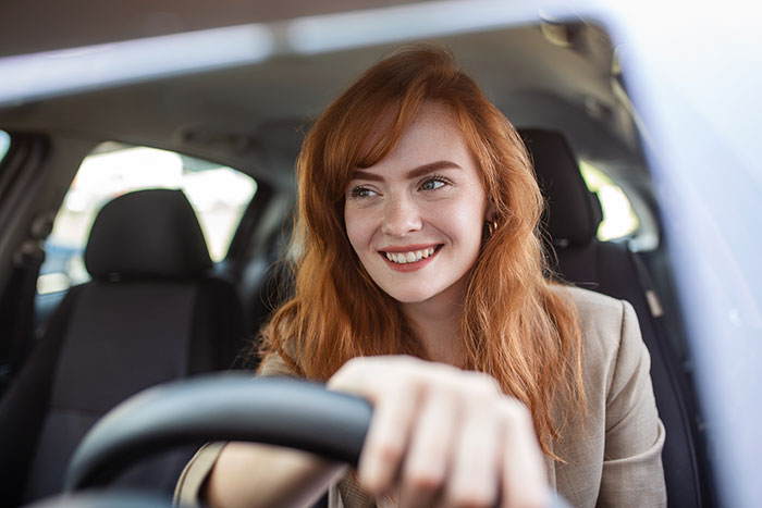 Young woman with red hair smiling while driving a car, symbolizing people who walked away from their old lives and started new ones