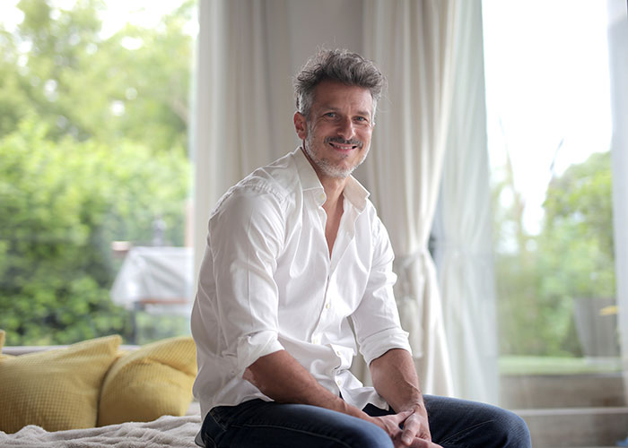 Middle-aged man sitting indoors near large window, symbolizing people who walked away from old lives and started anew.