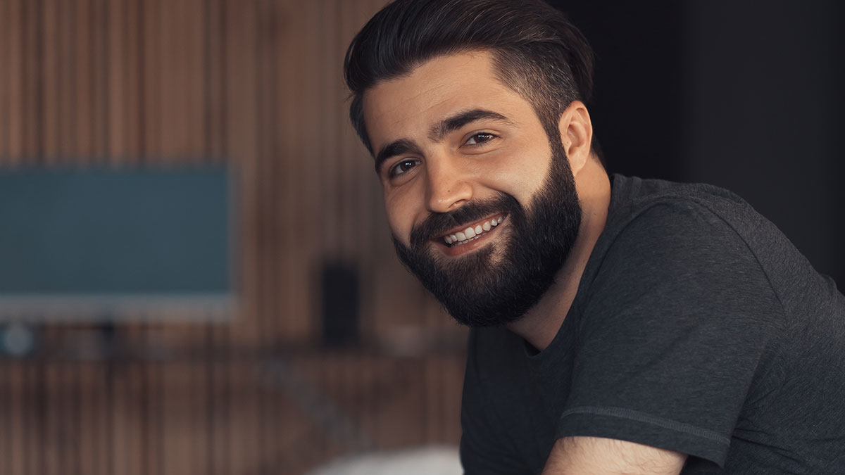 Smiling man with a beard in a casual dark shirt, representing people who walked away from their old lives and started new ones.