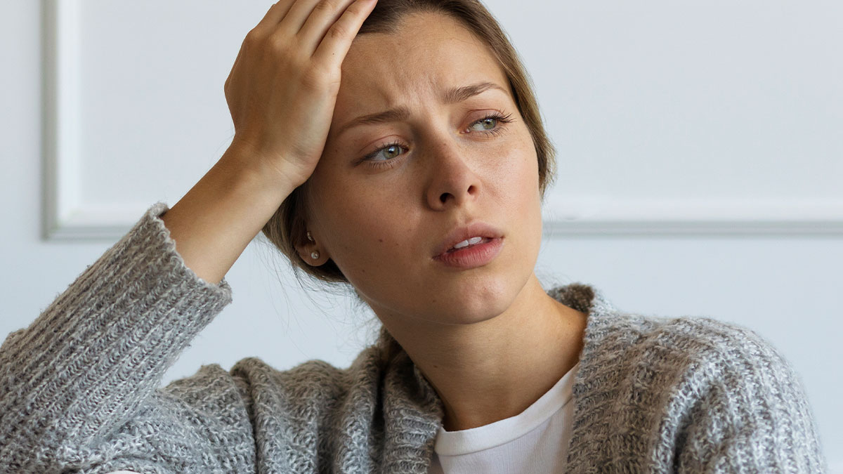 Worried woman in a gray sweater holding her head, showing an emotion that fits an Oscar-worthy performance.