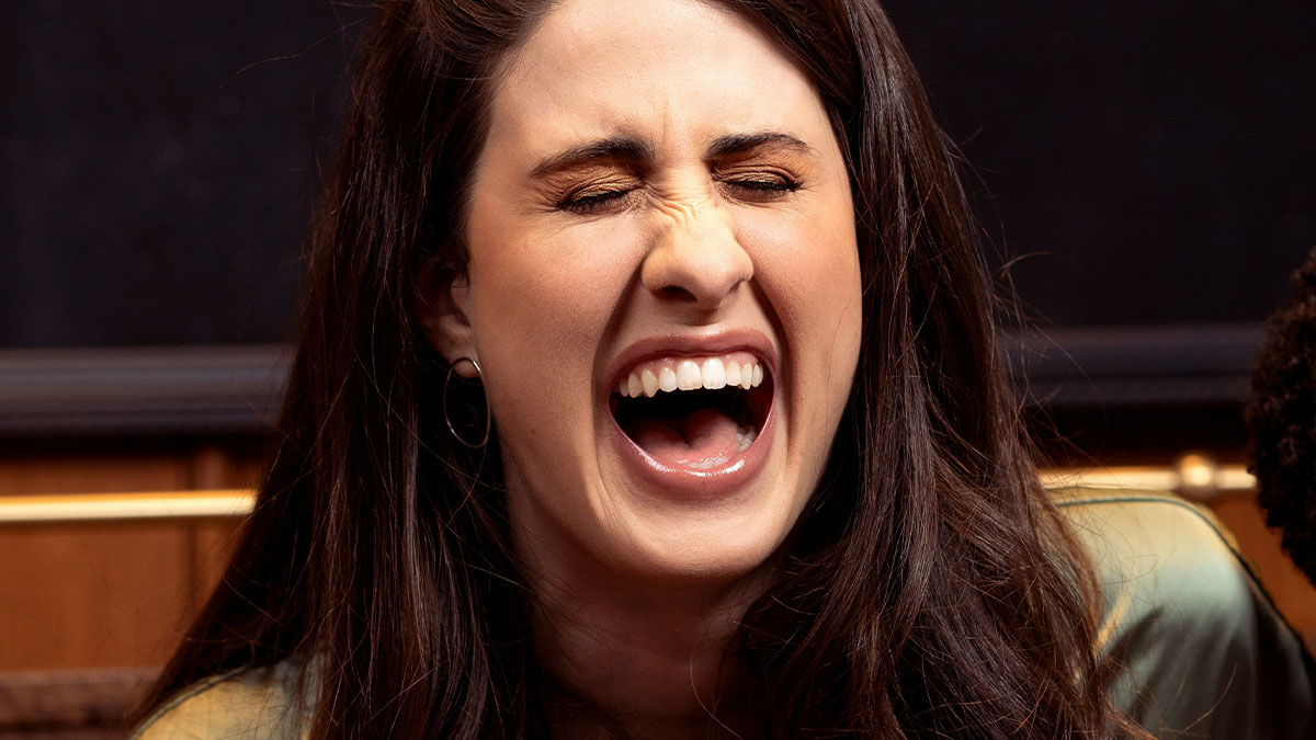 Young woman with long dark hair laughing joyfully, capturing a moment of instant karma shared among people.