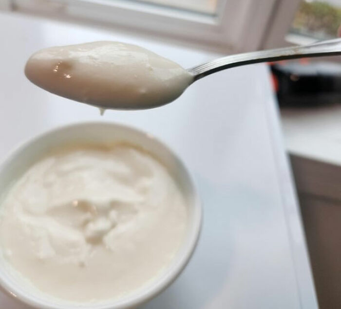 Close-up of creamy yogurt on a spoon above a white container showing kitchen tips and tricks to upgrade cooking skills. Close-up of creamy yogurt on a spoon above a white container showing kitchen tips and tricks to upgrade cooking skills.