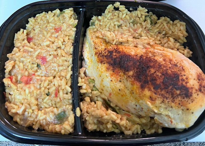 Close-up of a cooked chicken breast with seasoned rice in a divided black meal prep container, showcasing kitchen tips and tricks.