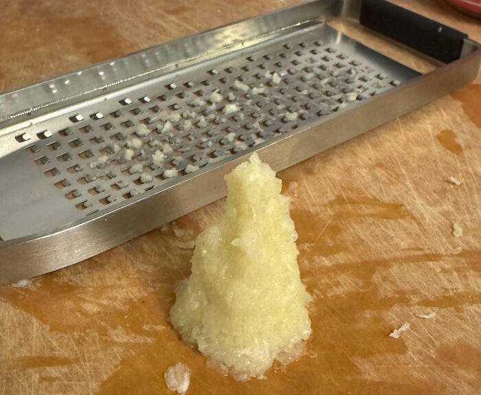 Fine garlic paste next to a metal grater on a wooden cutting board, showcasing kitchen tips and cooking skills.