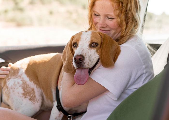 Young woman smiling while hugging her intelligent pet dog inside a car, showing a close bond between them.