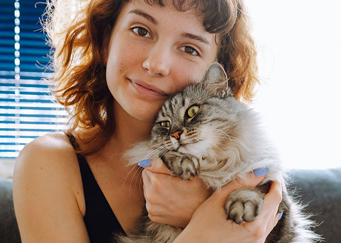 Young woman holding a fluffy cat, showcasing one of the most intelligent pets people have ever had in a cozy setting.