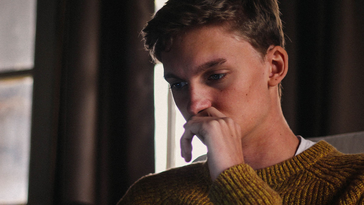 Young man looking anxious and picking at his food during dinner with momu2019s boss in a dimly lit room.