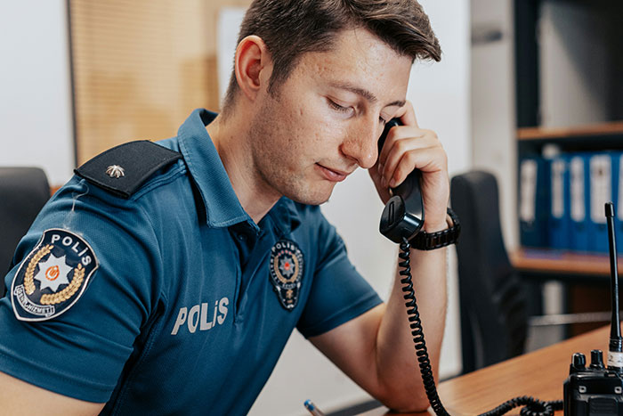 Police officer in uniform speaking on a landline phone, focused on a call in an office setting. Police officer in uniform speaking on a landline phone, focused on a call in an office setting.