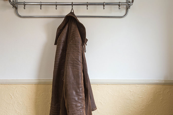Brown leather jacket hanging on a metal rack against a plain wall, related to coworker refusing to return expensive jacket. Brown leather jacket hanging on a metal rack against a plain wall, related to coworker refusing to return expensive jacket.
