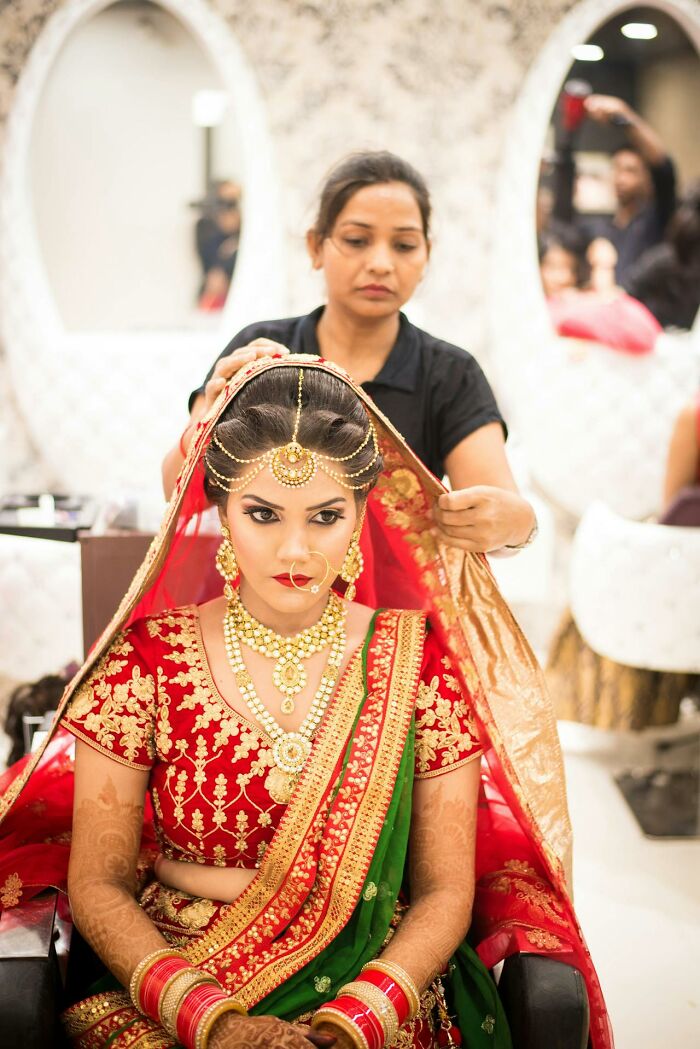Bride wearing traditional Indian jewelry and saree having her veil adjusted, capturing bizarre moments that made people wonder sanity.