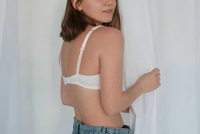 Young woman in a white bra and jeans pulling back a white curtain, illustrating optional choices in life.