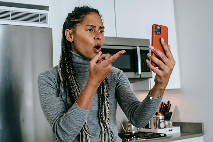 Woman with braided hair in gray turtleneck arguing on phone, showing frustration about homeless sister-in-law situation. Woman with braided hair in gray turtleneck arguing on phone, showing frustration about homeless sister-in-law situation.