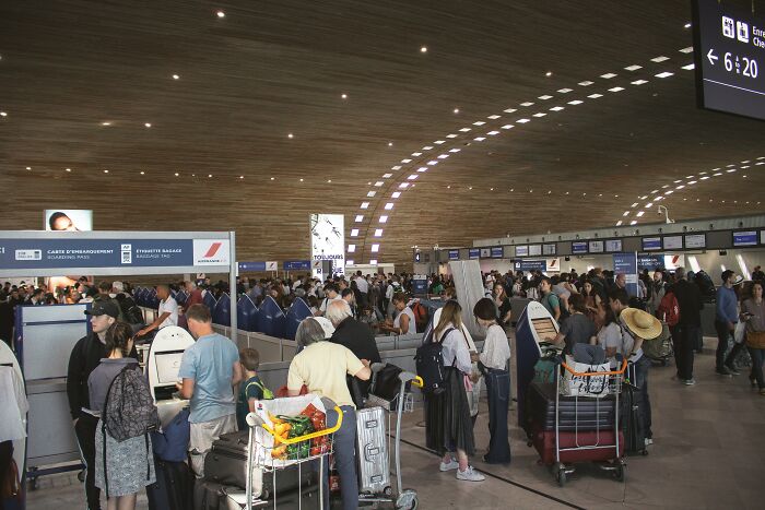 Busy airport check-in area filled with travelers experiencing one of the relatable but ridiculous everyday situations.