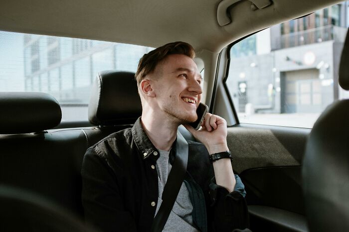 Young man smiling and talking on phone while sitting in backseat, capturing moments of realizing compulsory things are optional.