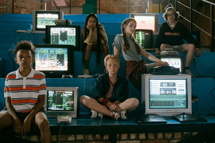 Group of kids with vintage computers and game consoles playing classic 80s and 90s references together indoors. Group of kids with vintage computers and game consoles playing classic 80s and 90s references together indoors.