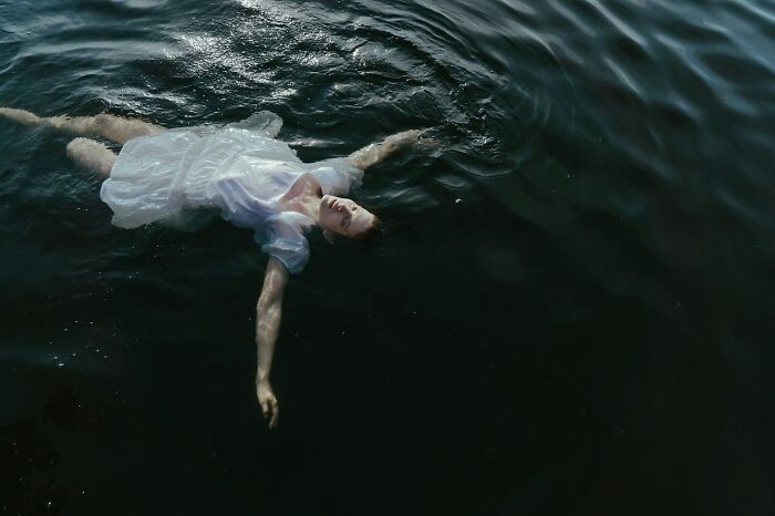 A person in a white dress floating peacefully in dark water, representing people who came back to life experiences.