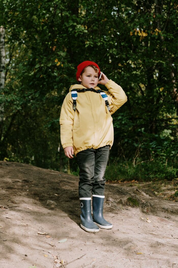 Child in yellow jacket and red hat standing outdoors in forest, capturing funny and serious moments parents raised monsters.