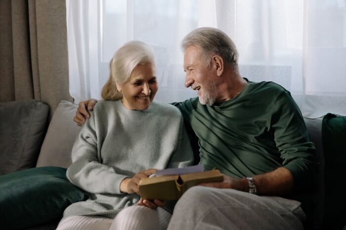 Older couple smiling and sitting together on a couch, reflecting on harsh truths about marriage and its reality.