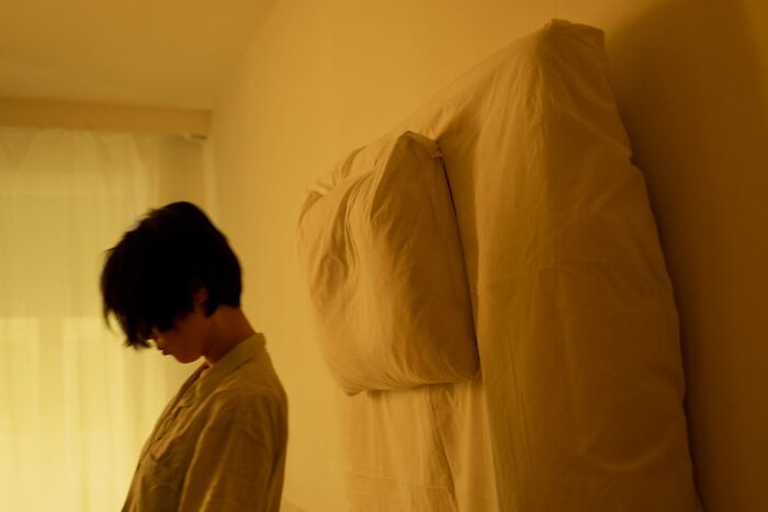 Person in soft light standing beside a bed, reflecting on experiences shared by people who came back to life.