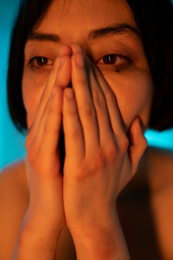 Close-up of a person covering their face with hands, expressing heavy emotions and confessions in a dimly lit setting.