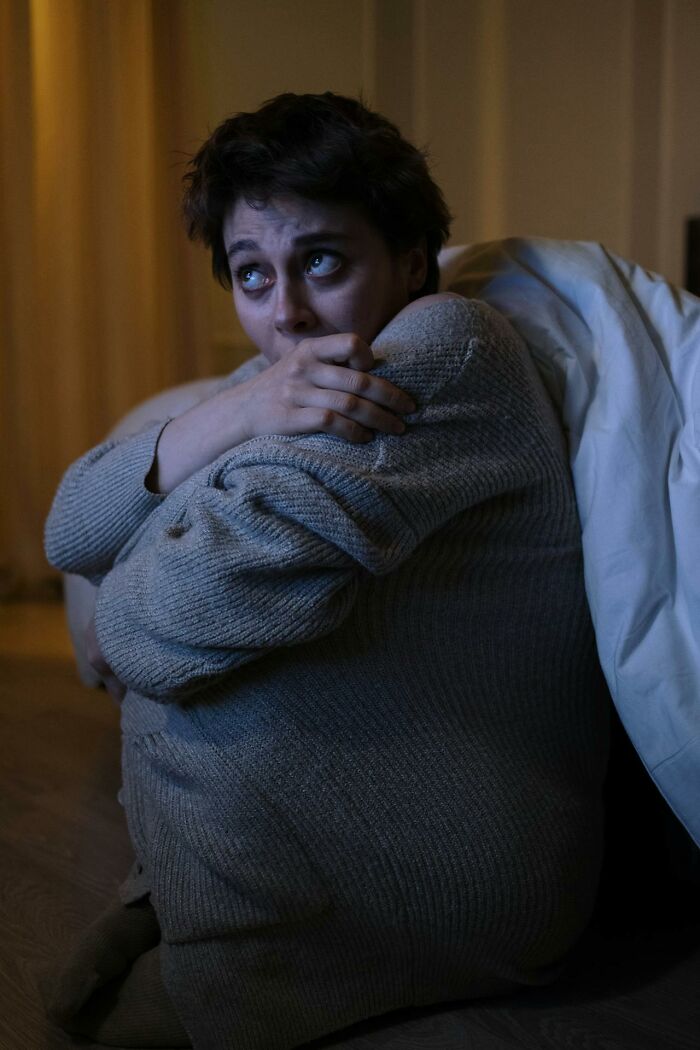 Person sitting on floor in a dimly lit room, hugging knees, portraying intense emotions related to psych ward nurses stories.