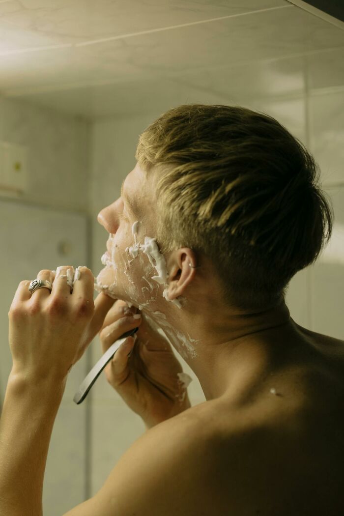 Young man shaving with razor in bathroom, capturing a funny and serious moment parents realized they were raising monsters