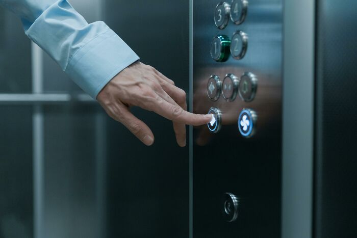 Person pressing elevator button in a modern elevator, illustrating relatable and ridiculous everyday habits we’re all guilty of.