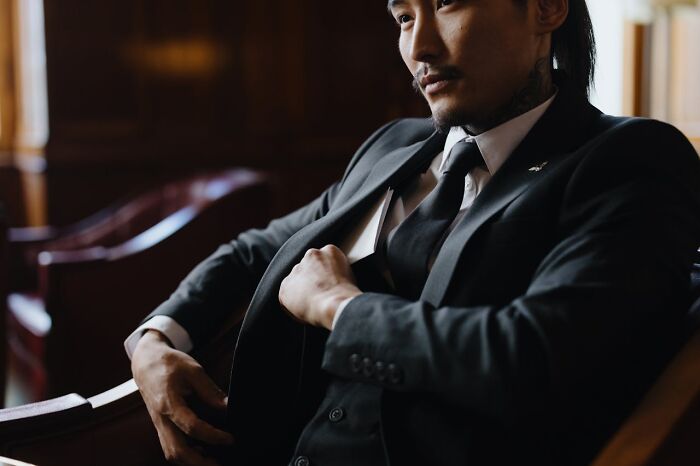 Man in a dark suit sitting thoughtfully in a leather chair, conveying intense and heavy confessions atmosphere.