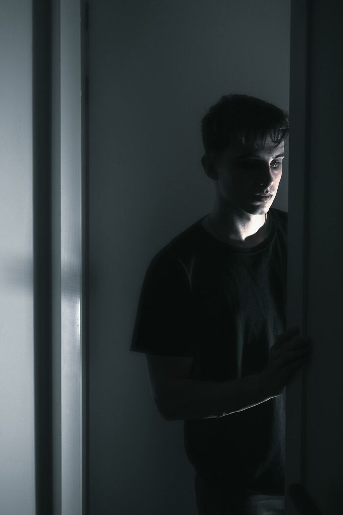 Young man in dark room partially lit, reflecting on experience related to dying and coming back to life.