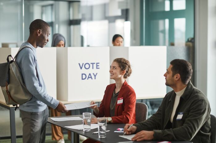Young man at a voting station interacting with election officials during vote day amid the bizarre moments.