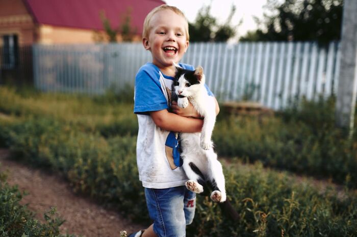 Happy child holding a black and white cat outdoors, capturing funny and serious moments of parents raising monsters.