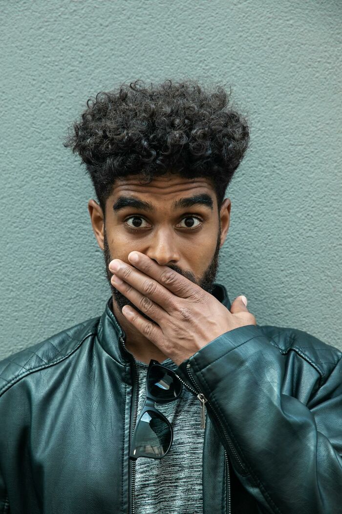 Man with curly hair in black leather jacket covering his mouth, symbolizing heavy confessions people refused to take to their graves.