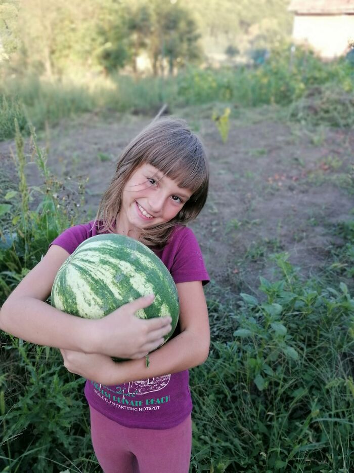 Smiling child holding a large watermelon outdoors, capturing a funny and serious moment of parents raising monsters.
