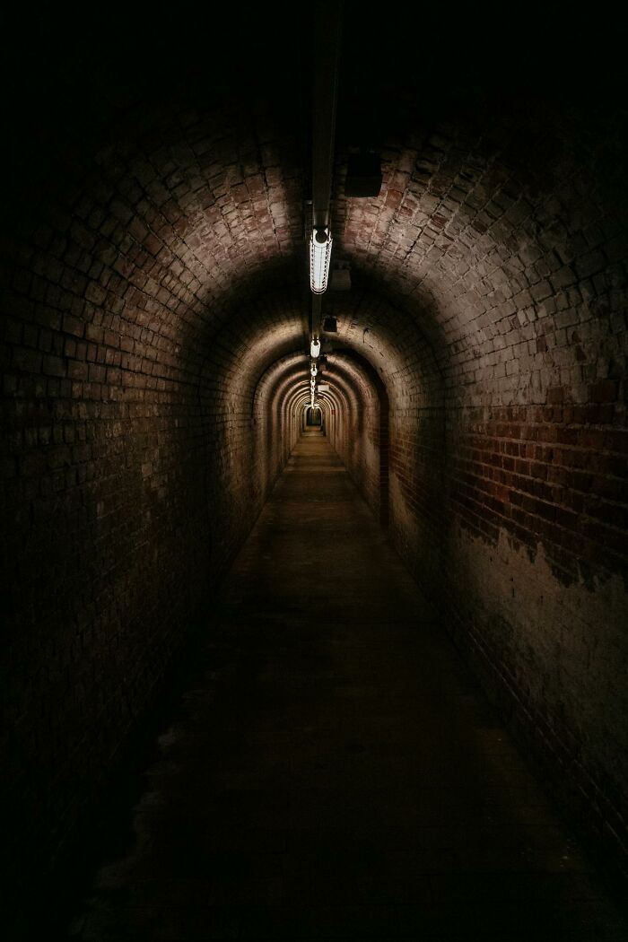 Dimly lit brick tunnel with overhead lights, evoking the feeling shared by people who came back to life after dying experiences.