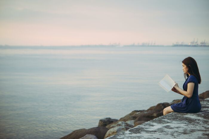 Woman in blue dress reading by the calm sea, reflecting on the correct spelling of embarrassed in a quiet setting Woman in blue dress reading by the calm sea, reflecting on the correct spelling of embarrassed in a quiet setting