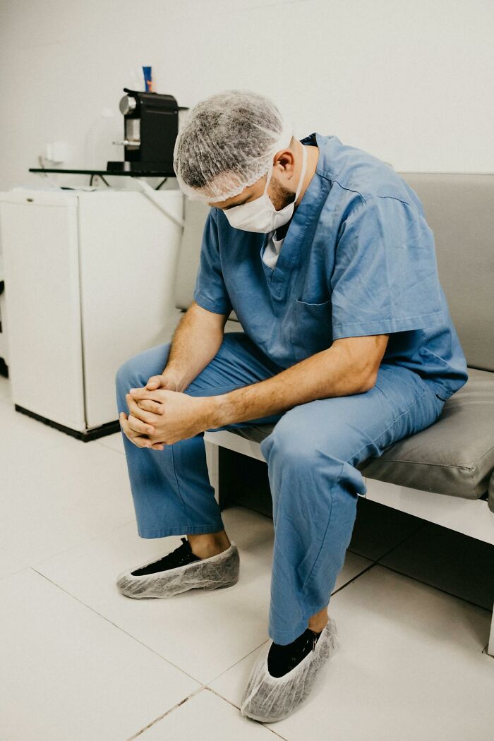 Male psych ward nurse in blue scrubs sitting and resting during a break showing intensity and fatigue.