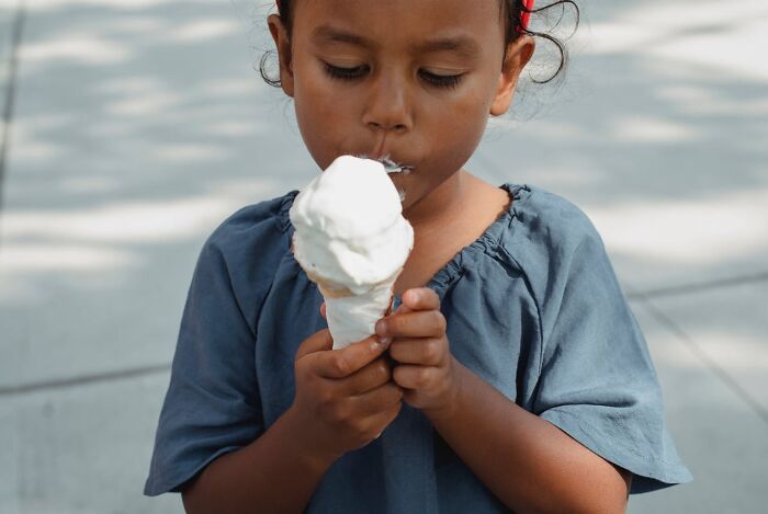 Young child carefully holding and eating a melting ice cream cone outdoors on a sunny day, showing Karen behavior.